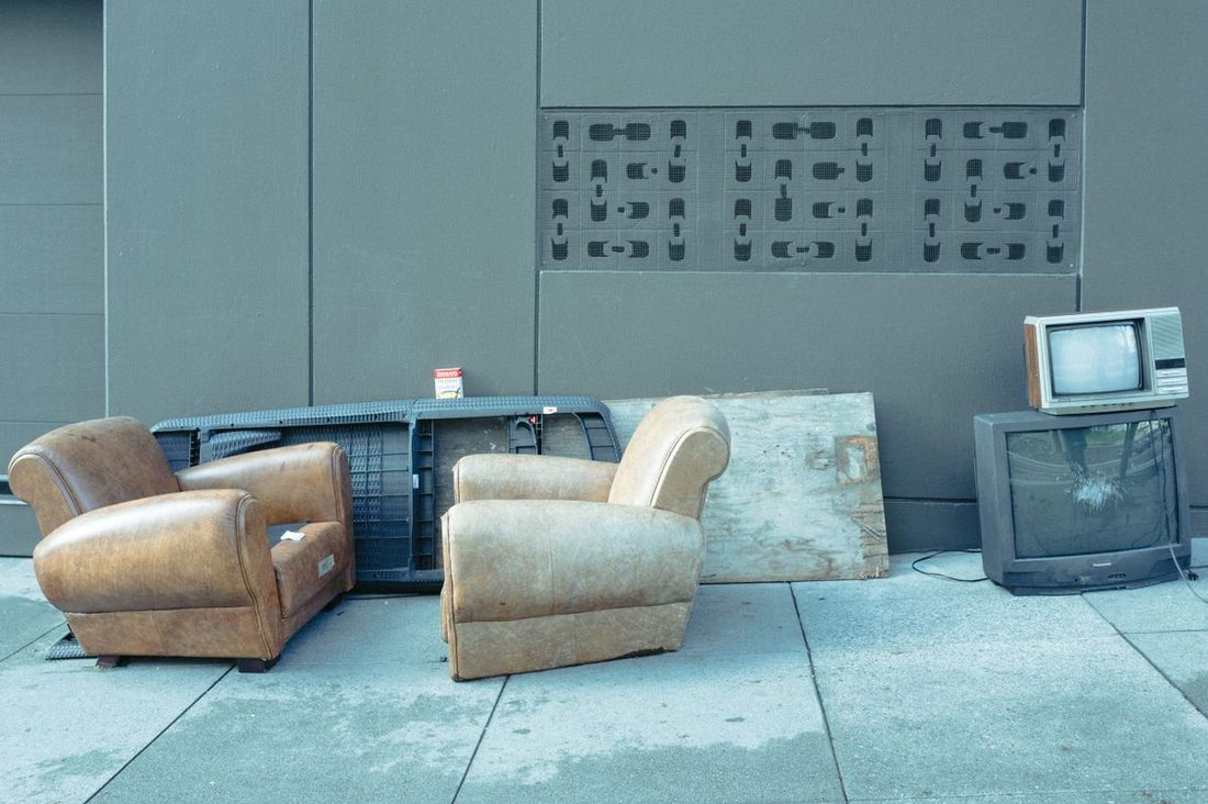 Worn leather armchairs and old televisions left at a curb for pickup
